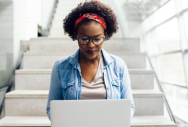 Female college student sitting on steps working on a laptop