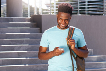 Male college student standing in front of steps looking at a smart phone