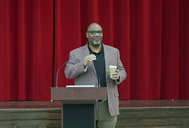 President Edington standing at a podium with a coffee cup in his hand, speaking.