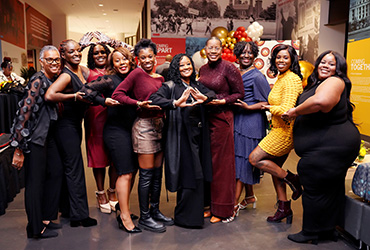 A group of women standing around a table making sorority hand signs.