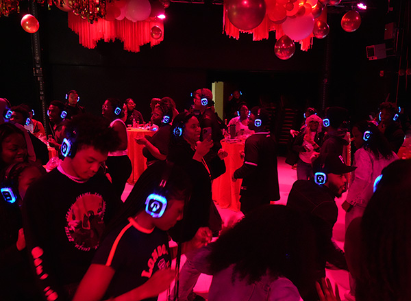 A group of people dancing in a darkly lit room wearing glowing headphones.