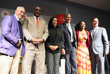 A group of people standing on a stage wearing business attire smiling.