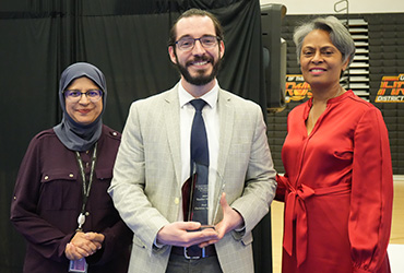 Man holding an award with a woman standing next to him on both sides