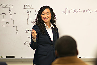 female teacher standing in front of a white board that has formulas on it