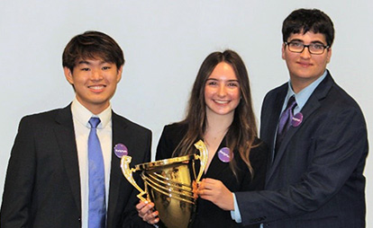 Three students wearing suits holding a trophy