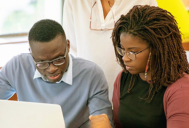 A woman tutoring a man at a laptop