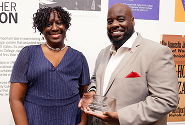 A woman and man smiling. The man is holding an award.