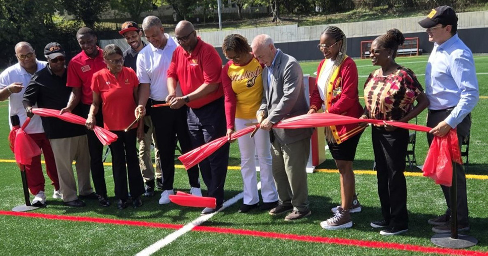 A group of people cutting a red ribbon on a new athletic turf field