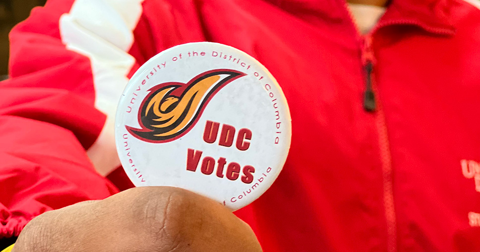 Student holding a patch that reads UDC Votes