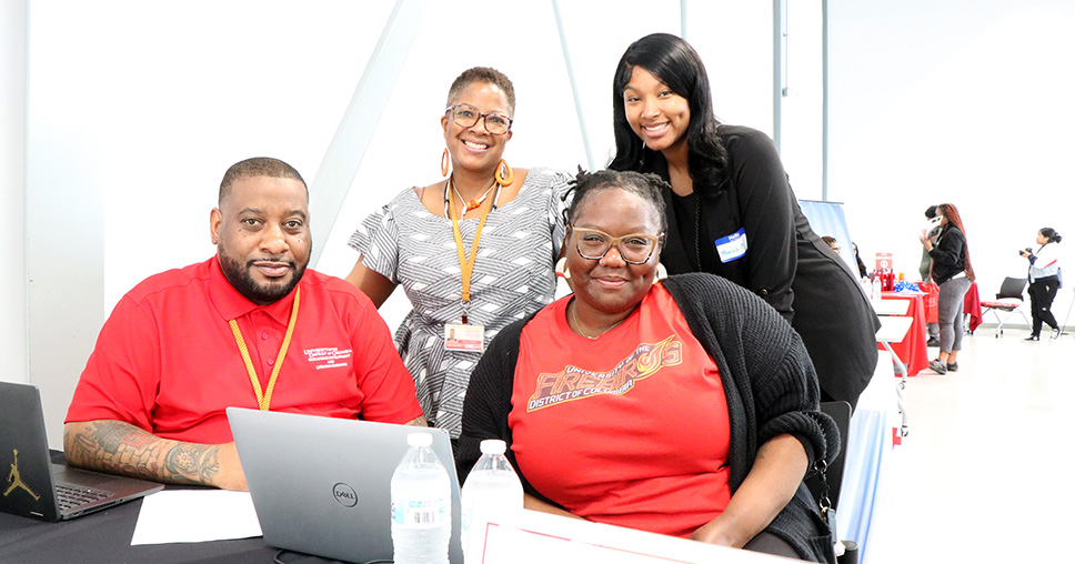 4 people sitting at a registration booth smiling